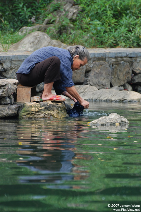 A old woman washing clothes in Yao River, Huangyao, Guangxi